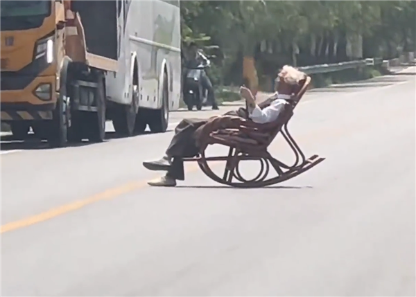 大爷马路中间手拿折扇躺摇椅上晒太阳 过往车辆纷纷减速避让